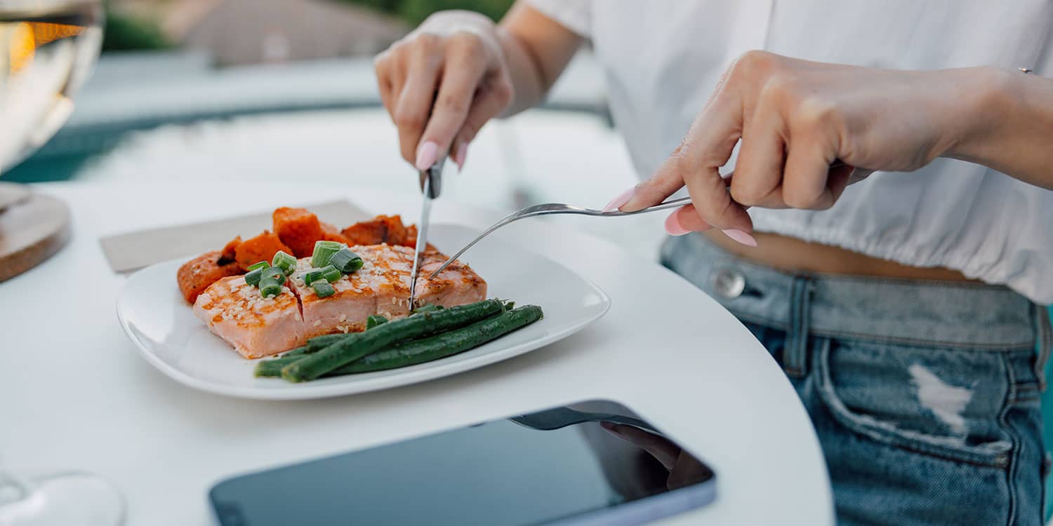 Hands cutting salmon with green beans and roasted sweet potatoes, an anti-inflammatory diet dinner plate.